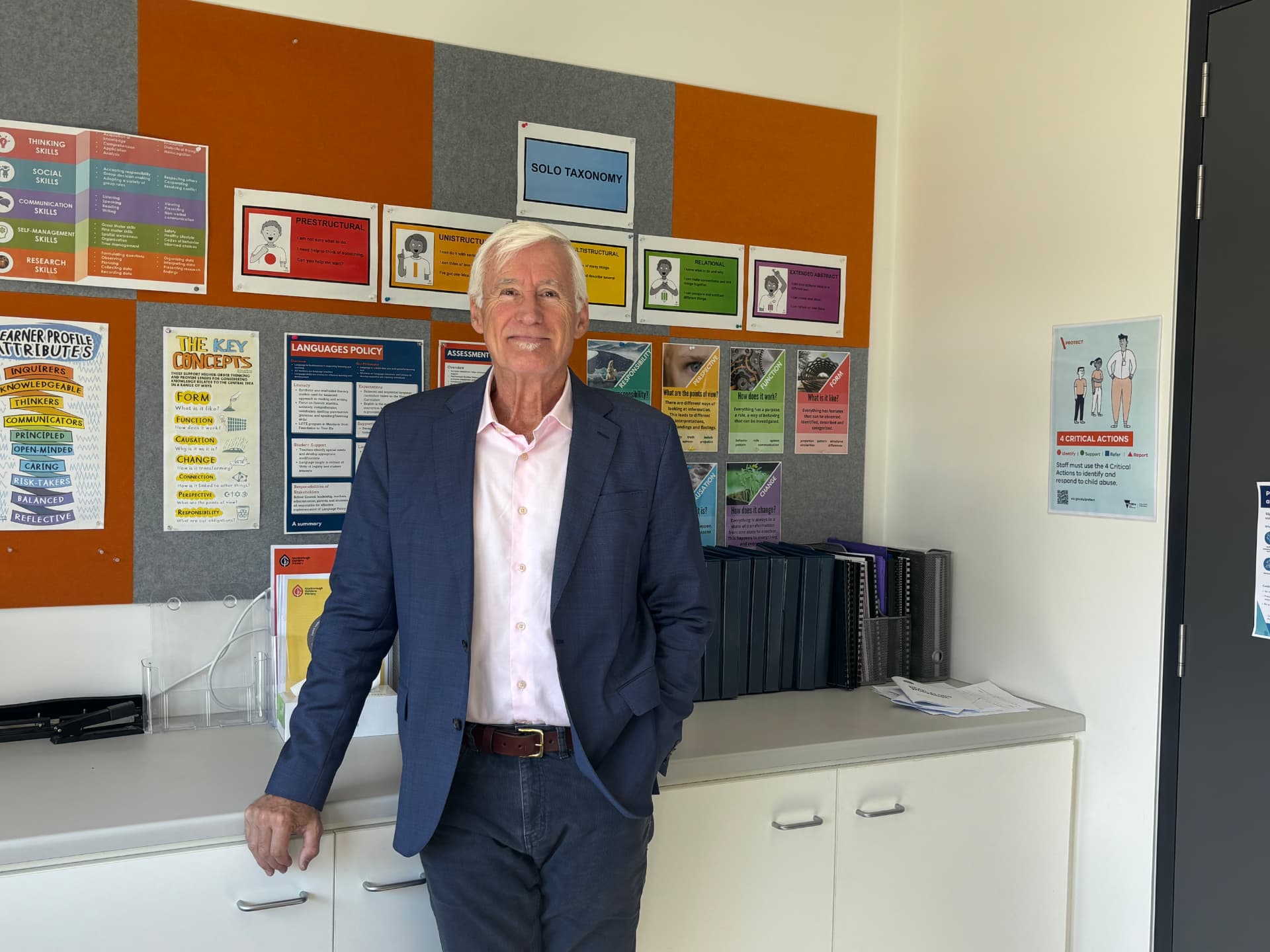 Phil Anthony standing in a school office in front of a wall of learning posters
