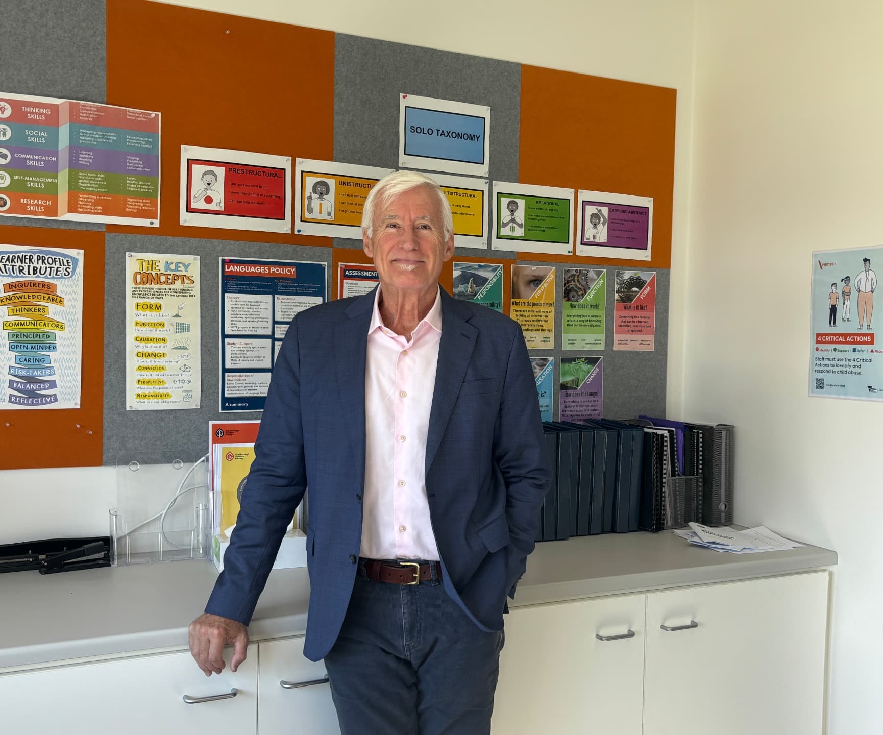 Phil Anthony standing in a school office in front of a wall of learning posters